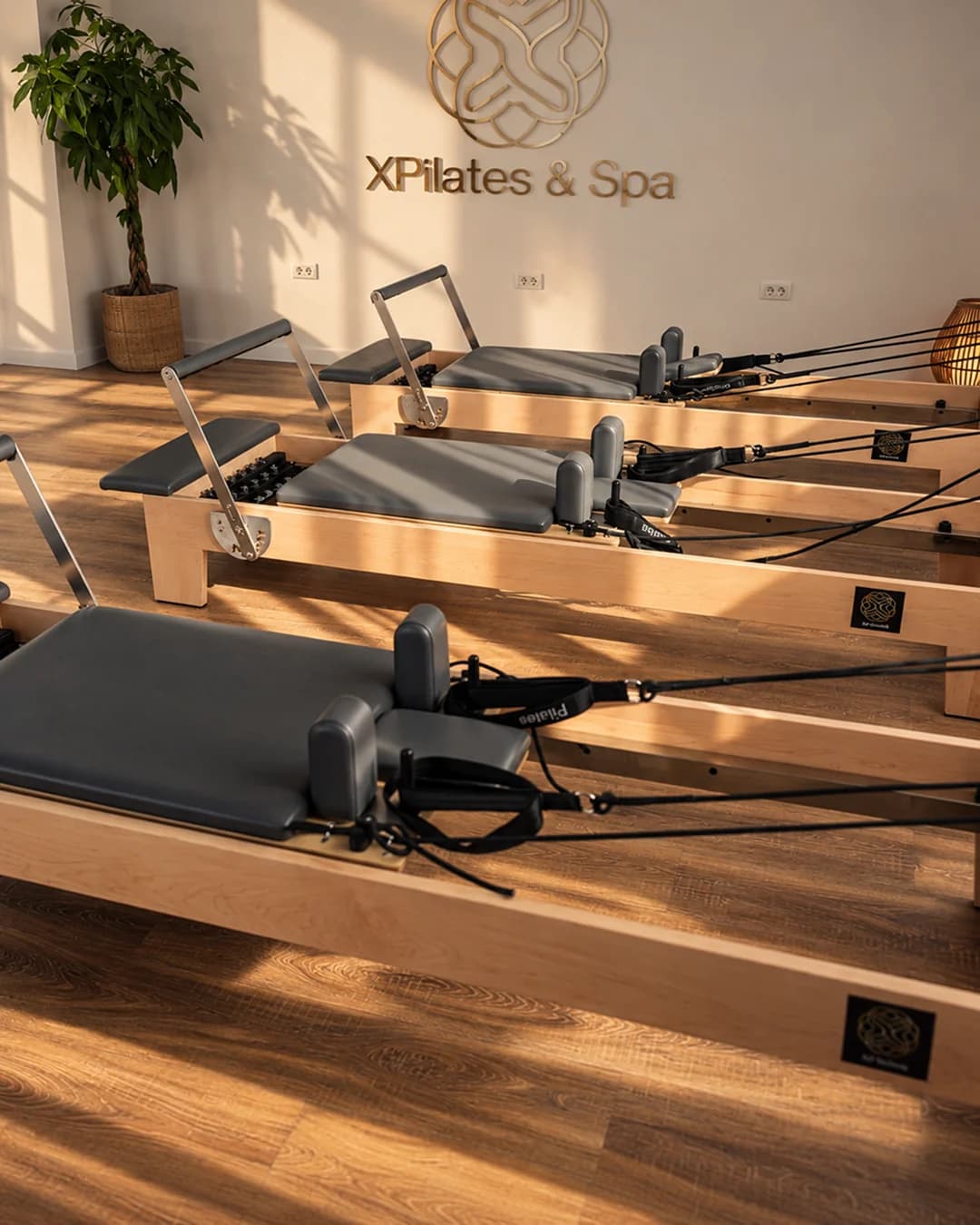 Aparatele Pilates Reformer și sigla XPilates & Spa în lumina caldă a studioului